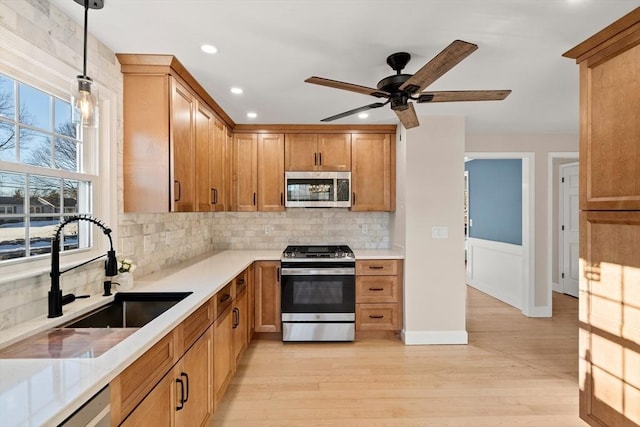 kitchen featuring pendant lighting, sink, backsplash, stainless steel appliances, and light hardwood / wood-style floors