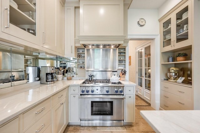 kitchen with light tile patterned flooring, light stone countertops, premium range hood, and stainless steel stove