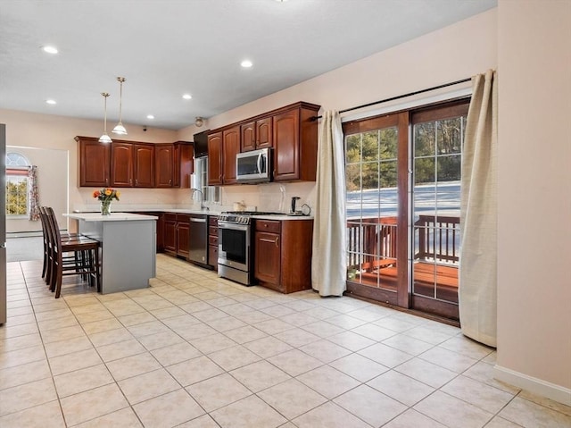 kitchen with appliances with stainless steel finishes, hanging light fixtures, a kitchen breakfast bar, a healthy amount of sunlight, and a kitchen island