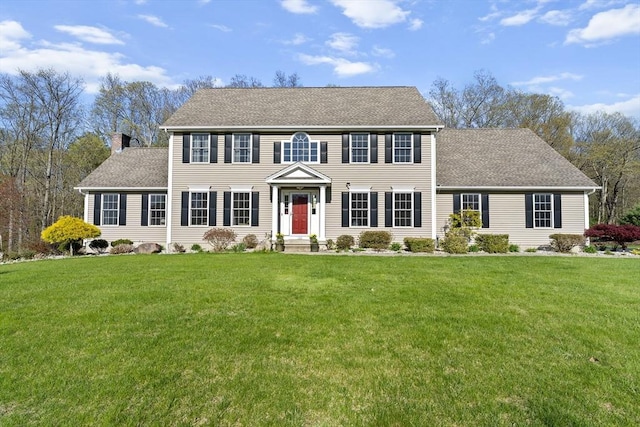 colonial inspired home with roof with shingles and a front lawn