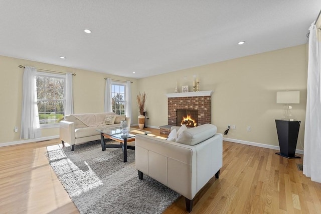 living room featuring a brick fireplace, recessed lighting, baseboards, and light wood finished floors