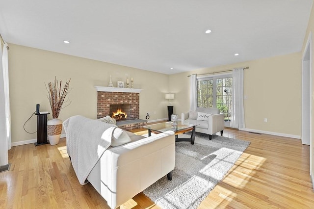 living area featuring baseboards, recessed lighting, light wood-style flooring, and a brick fireplace