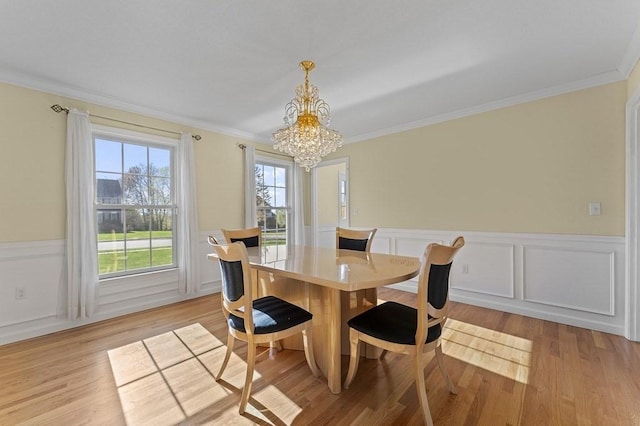 dining area featuring crown molding, a chandelier, wainscoting, and light wood finished floors