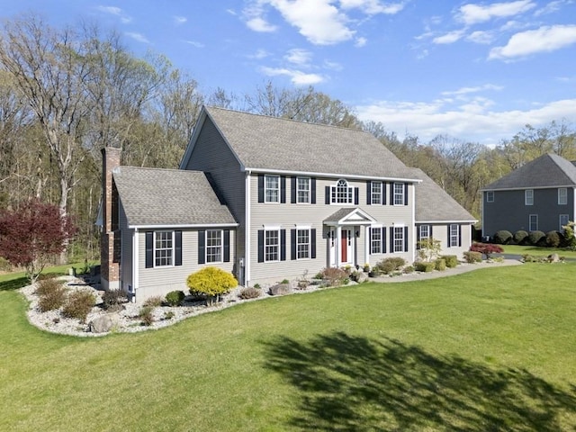 colonial-style house with roof with shingles, a chimney, and a front yard
