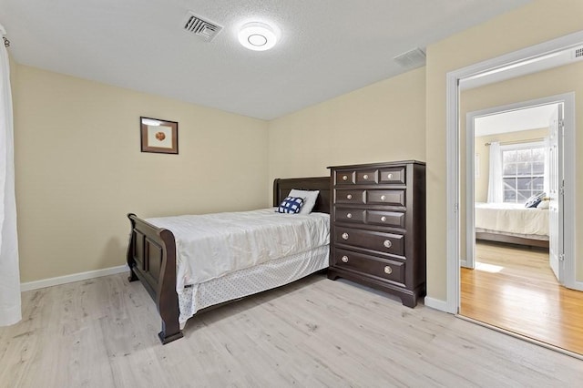 bedroom with baseboards, light wood finished floors, and visible vents