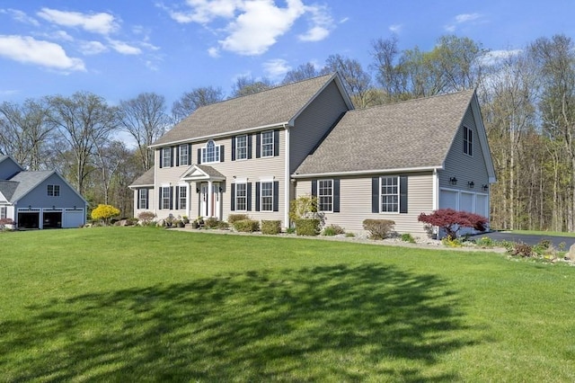 colonial inspired home featuring roof with shingles, an attached garage, and a front yard