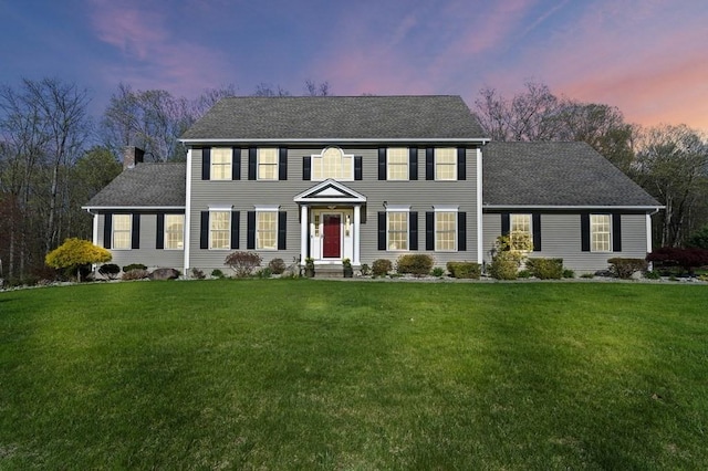 colonial-style house featuring a shingled roof, a yard, and a chimney