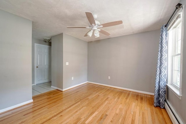empty room with a baseboard radiator, ceiling fan, light wood-style flooring, and baseboards