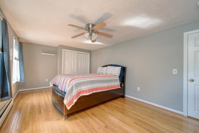 bedroom with baseboard heating, baseboards, light wood-style flooring, a closet, and a ceiling fan