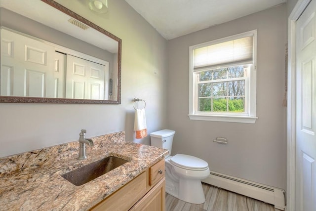 half bath featuring baseboard heating, toilet, wood finished floors, and vanity