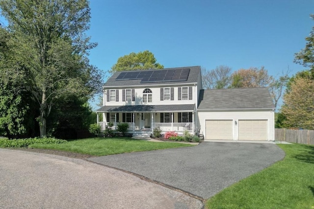 colonial inspired home with a porch, an attached garage, asphalt driveway, and roof mounted solar panels