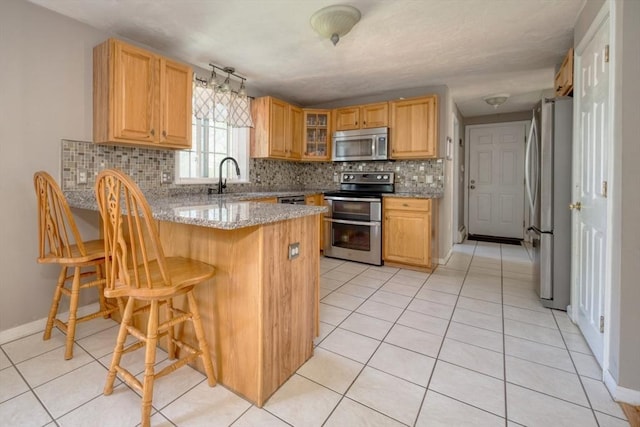 kitchen with appliances with stainless steel finishes, a peninsula, decorative backsplash, glass insert cabinets, and a breakfast bar