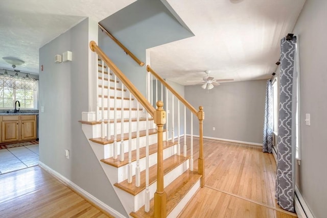 staircase with a baseboard radiator, wood finished floors, a ceiling fan, and baseboards