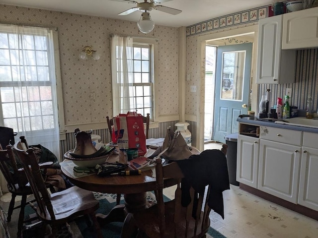 dining room featuring a wainscoted wall, a ceiling fan, and wallpapered walls
