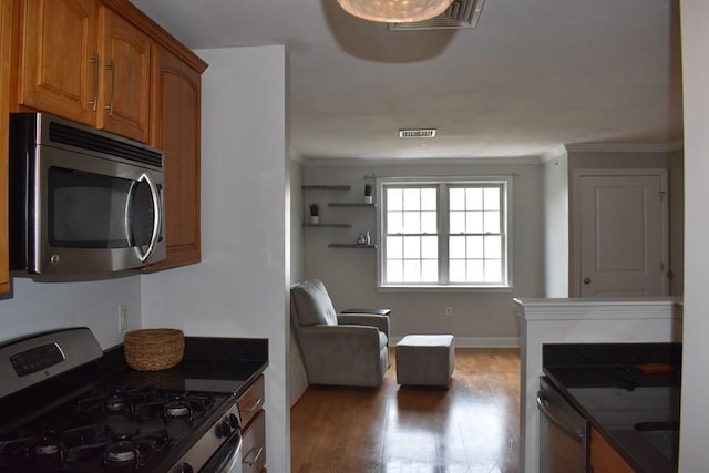 kitchen featuring brown cabinets, stainless steel appliances, dark countertops, visible vents, and wood finished floors