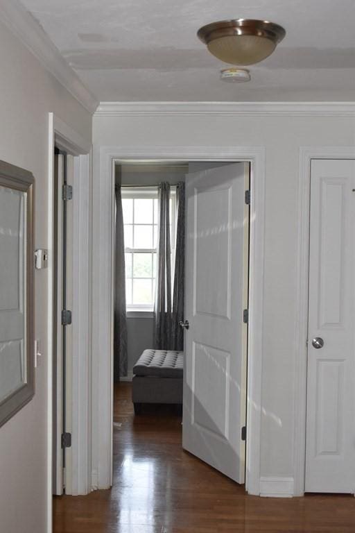 corridor with ornamental molding and wood finished floors