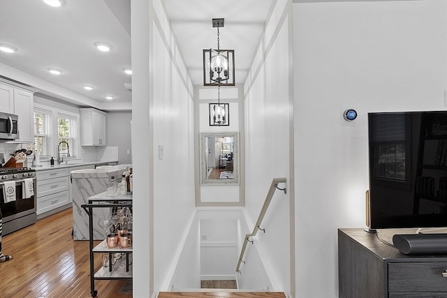 kitchen featuring appliances with stainless steel finishes, an inviting chandelier, hanging light fixtures, white cabinets, and light wood-type flooring