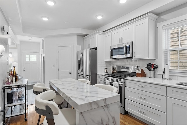 kitchen featuring backsplash, appliances with stainless steel finishes, light hardwood / wood-style floors, white cabinets, and a center island