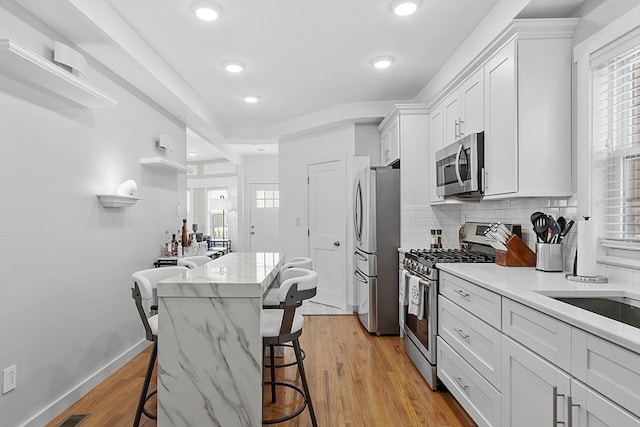 kitchen with light hardwood / wood-style floors, appliances with stainless steel finishes, a kitchen breakfast bar, a center island, and white cabinets