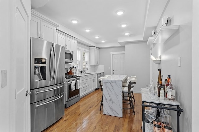 kitchen featuring stainless steel appliances, light hardwood / wood-style floors, white cabinetry, sink, and a kitchen breakfast bar