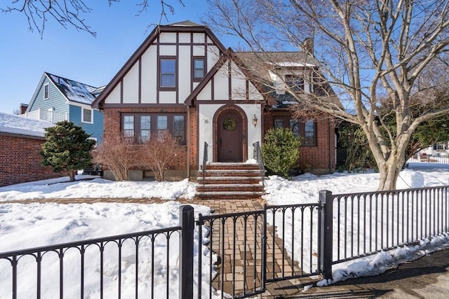 tudor-style house featuring a fenced front yard, a gate, and brick siding