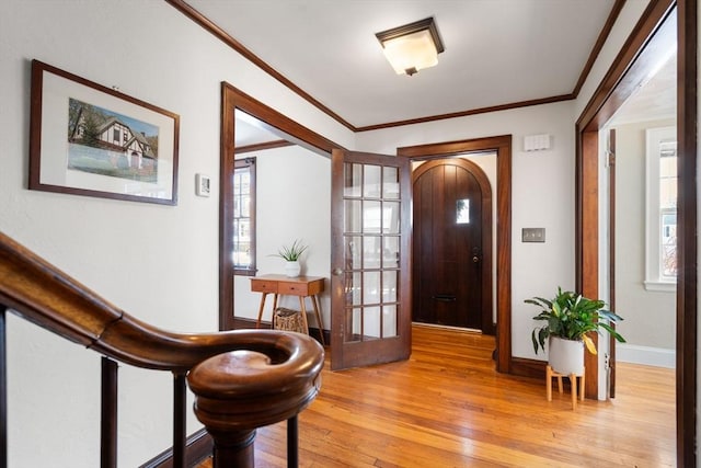 foyer entrance with ornamental molding, light wood-type flooring, arched walkways, and baseboards