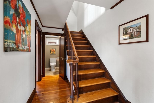 stairs featuring baseboards, wood-type flooring, and crown molding