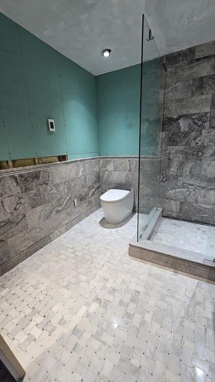 bathroom featuring toilet, tiled shower, and tile walls