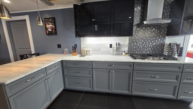 kitchen featuring stainless steel gas cooktop, wall chimney range hood, gray cabinetry, and hanging light fixtures