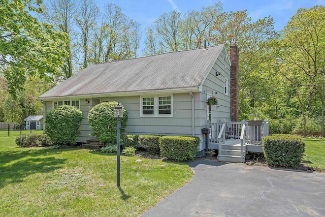 view of side of property with a lawn, a chimney, a deck, and roof with shingles