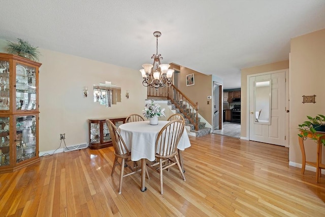 dining room with a chandelier, light wood-style flooring, baseboards, and stairs