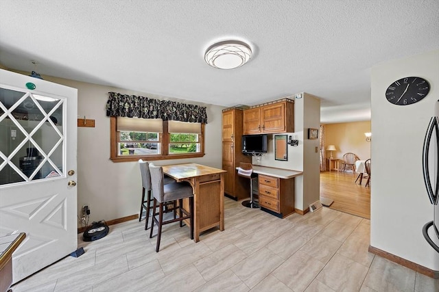 kitchen with brown cabinets, a textured ceiling, baseboards, and refrigerator