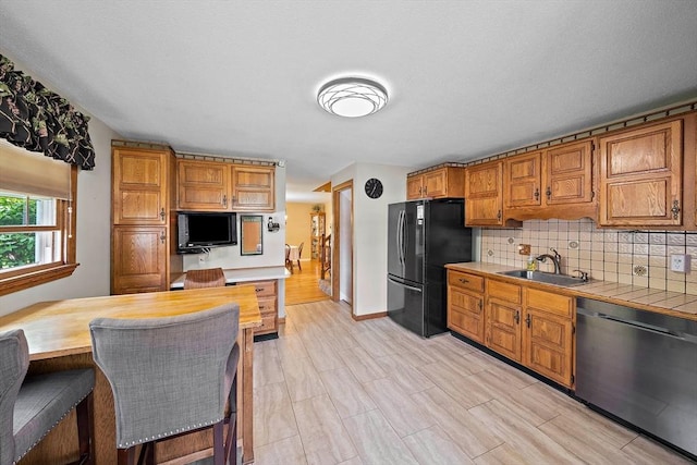 kitchen featuring stainless steel dishwasher, freestanding refrigerator, a sink, tile countertops, and brown cabinets