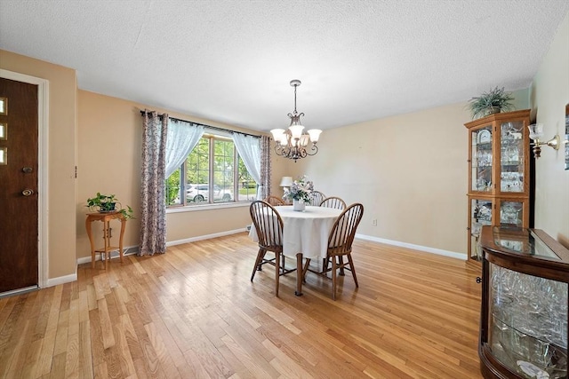 dining room with a chandelier, light wood-style flooring, a textured ceiling, and baseboards