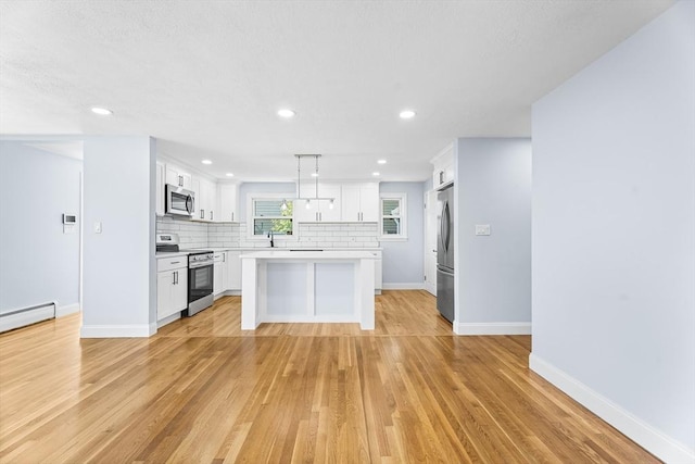 69 Kingman Ave, Revere, MA 02151 - kitchen with stainless steel appliances, light countertops, backsplash, a center island, and white cabinets