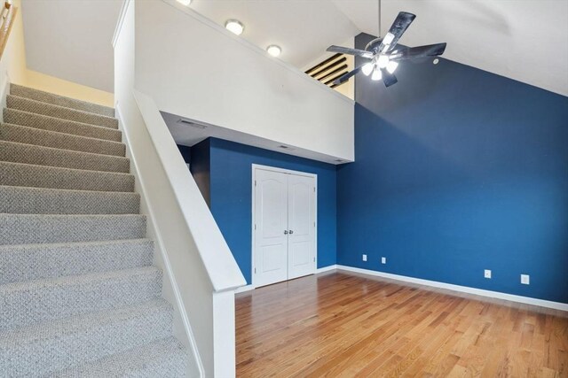 staircase featuring wood finished floors, a ceiling fan, high vaulted ceiling, and baseboards