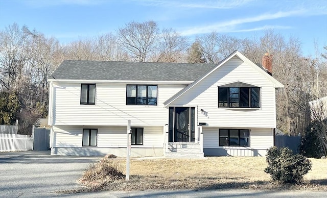 bi-level home featuring roof with shingles, a chimney, and fence