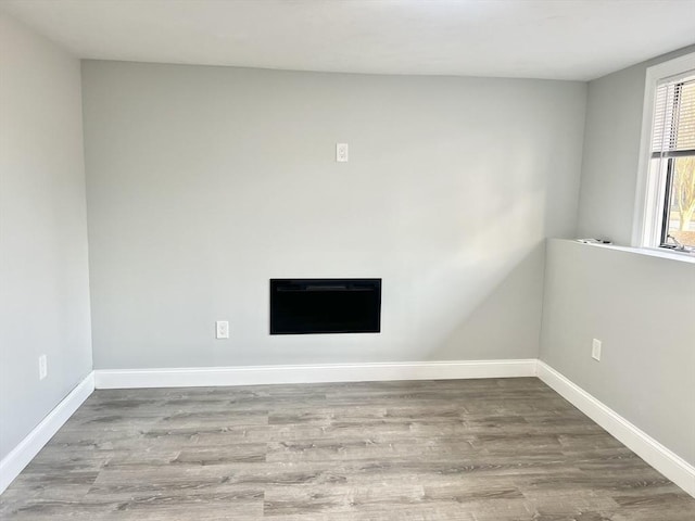 unfurnished living room with baseboards, heating unit, and wood finished floors