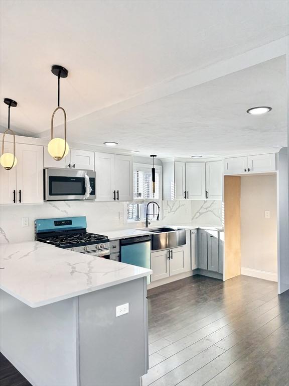 kitchen featuring light stone counters, appliances with stainless steel finishes, white cabinetry, wood finished floors, and a peninsula