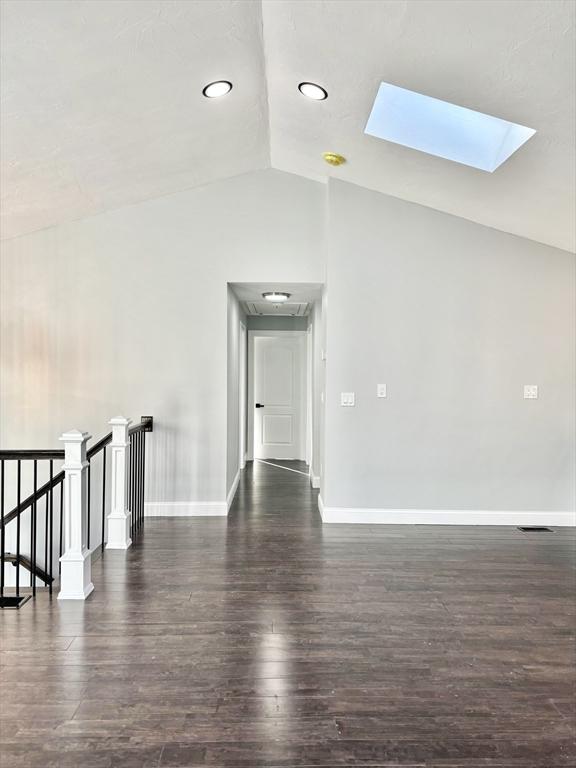 spare room with lofted ceiling with skylight, baseboards, and dark wood-style flooring