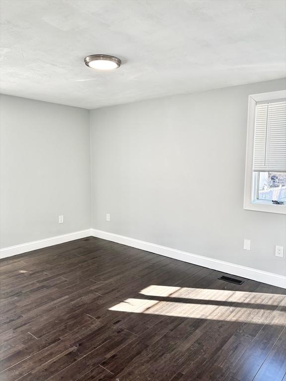 unfurnished room featuring dark wood-type flooring, visible vents, and baseboards