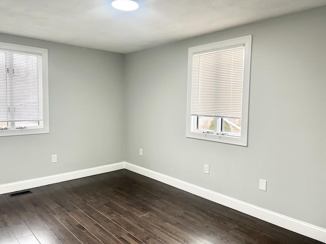 spare room with dark wood-style floors, visible vents, and baseboards