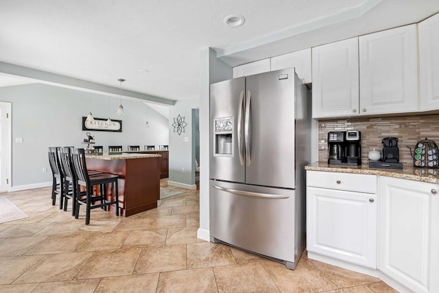 kitchen featuring pendant lighting, stainless steel fridge, a breakfast bar, white cabinetry, and decorative backsplash