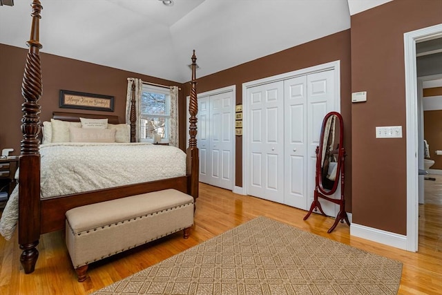 bedroom with vaulted ceiling, hardwood / wood-style floors, and two closets