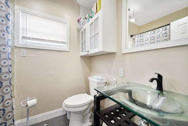 full bath featuring curtained shower, baseboards, toilet, wood finished floors, and a sink