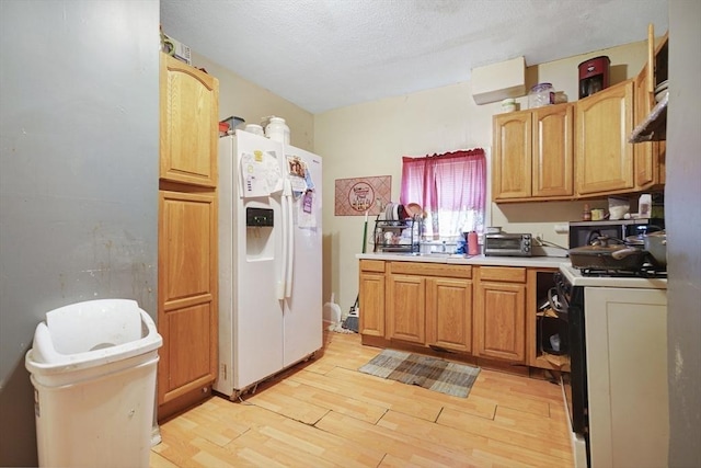 kitchen with under cabinet range hood, gas stove, light wood-style floors, white fridge with ice dispenser, and light countertops