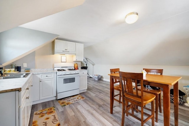 kitchen with light wood-style flooring, under cabinet range hood, white gas range oven, white cabinetry, and vaulted ceiling