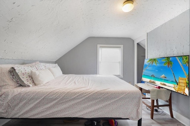 bedroom with lofted ceiling, wood finished floors, baseboards, and a textured ceiling