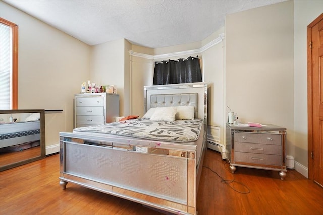 bedroom featuring a baseboard radiator, a textured ceiling, baseboards, and wood finished floors