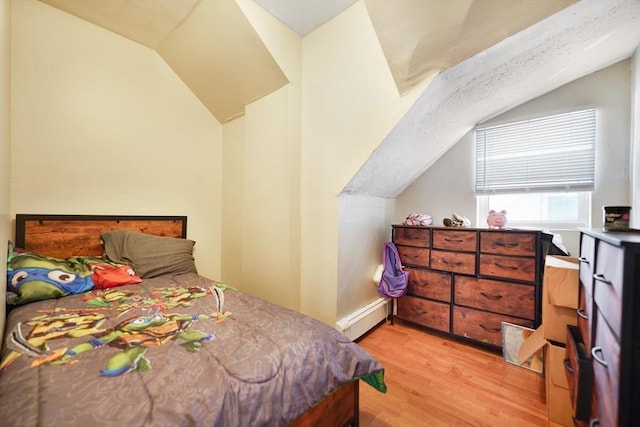 bedroom with baseboard heating, light wood-style flooring, and vaulted ceiling